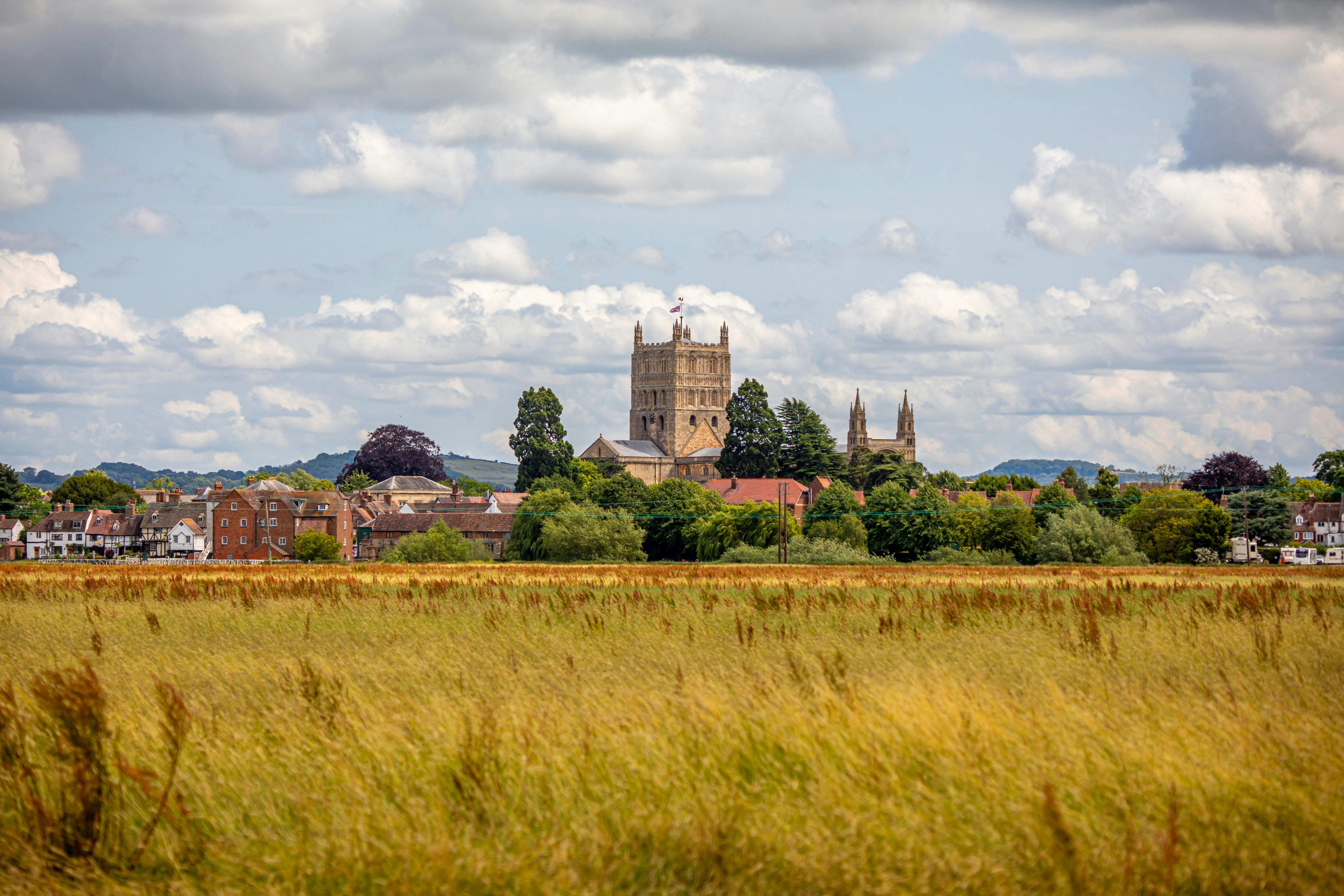 Scenic view of Tewkesbury Abbey surrounded by lush greenery and dramatic clouds. Perfect for travel and architecture themes.