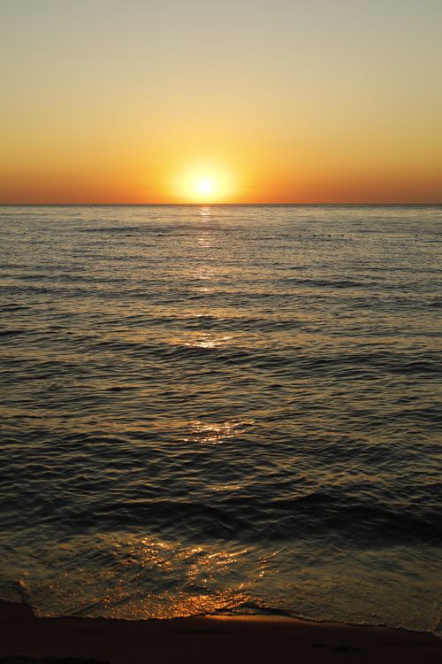 Free A tranquil sunset over the ocean with golden reflective waters. Stock Photo