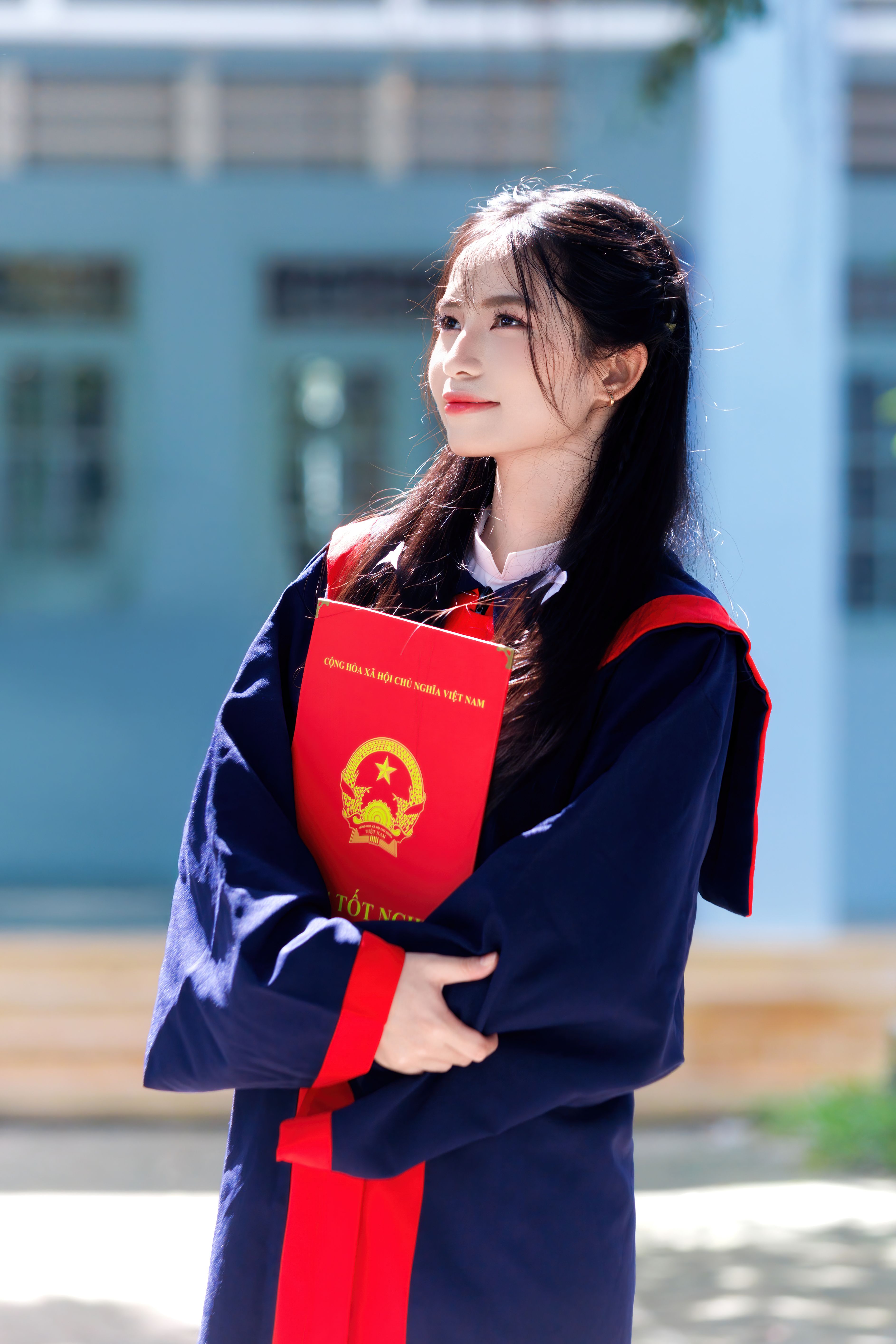 Young woman in graduation gown holding a red certificate, celebrating academic success.