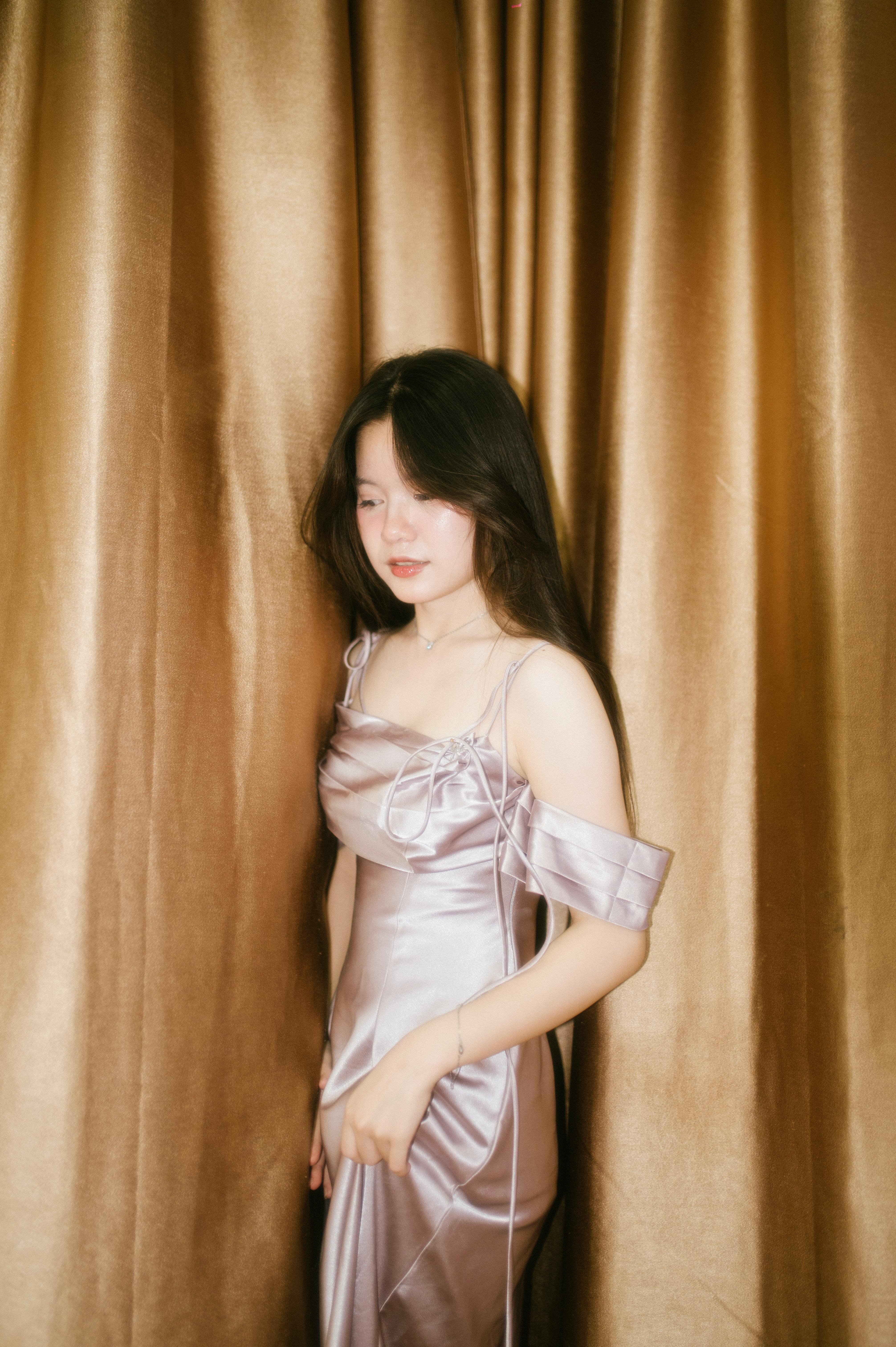 A serene portrait of a woman in a satin gown set against luxurious golden curtains.