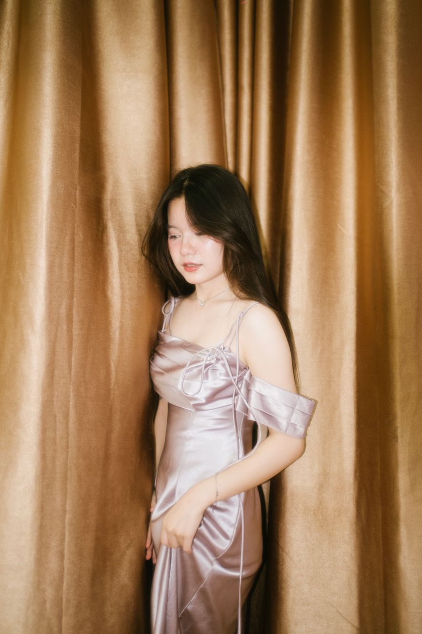 A serene portrait of a woman in a satin gown set against luxurious golden curtains.
