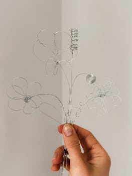 Minimalist wire flowers held by hand against a neutral background, emphasizing creative craftsmanship.