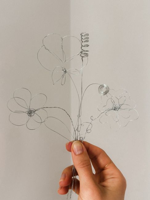 Minimalist wire flowers held by hand against a neutral background, emphasizing creative craftsmanship.