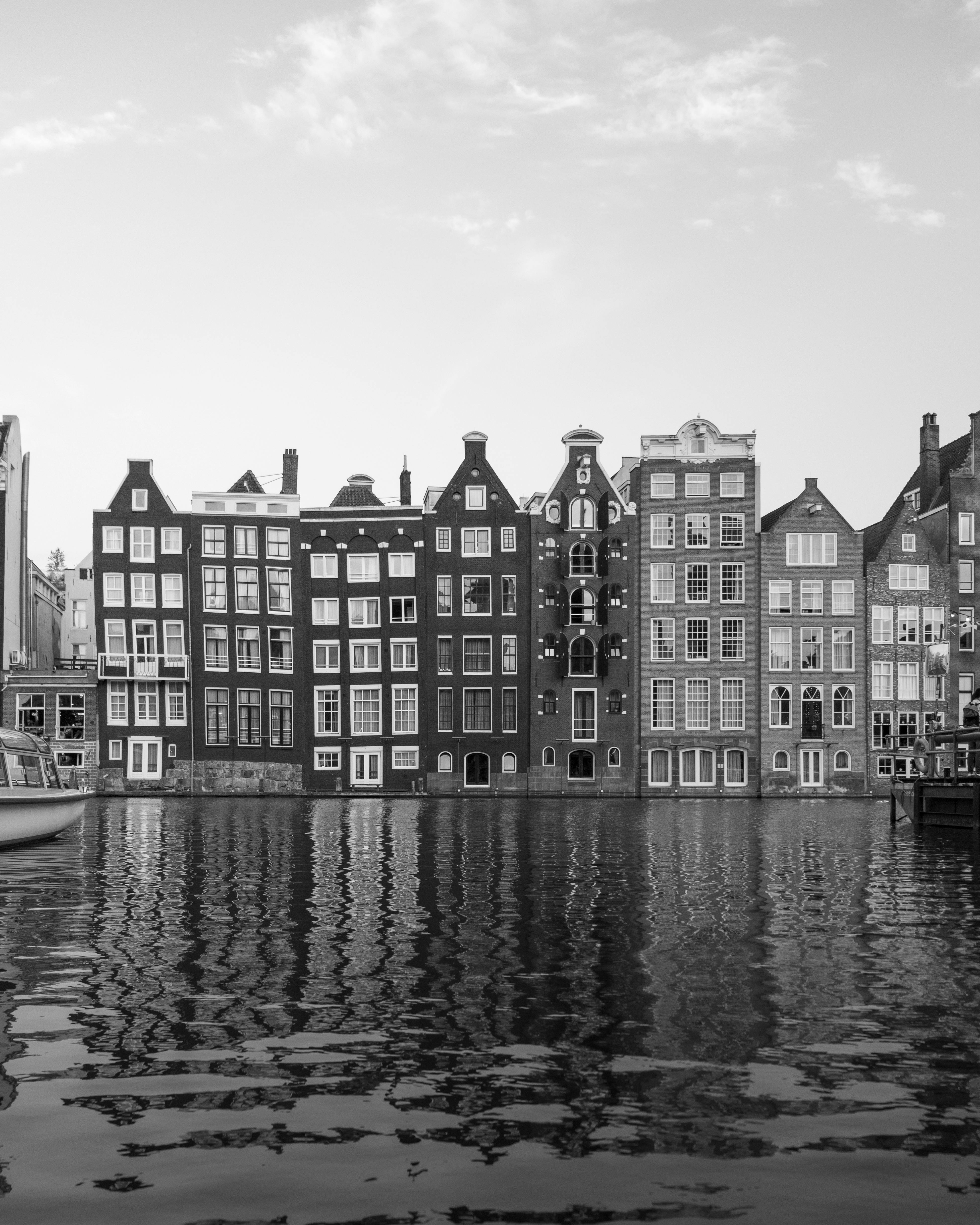 Black and white image of Amsterdam's iconic canal houses reflecting in water, a hallmark of Dutch architecture.