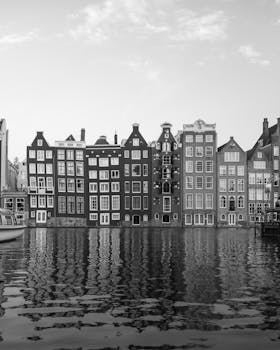 Black and white image of Amsterdam's iconic canal houses reflecting in water, a hallmark of Dutch architecture.