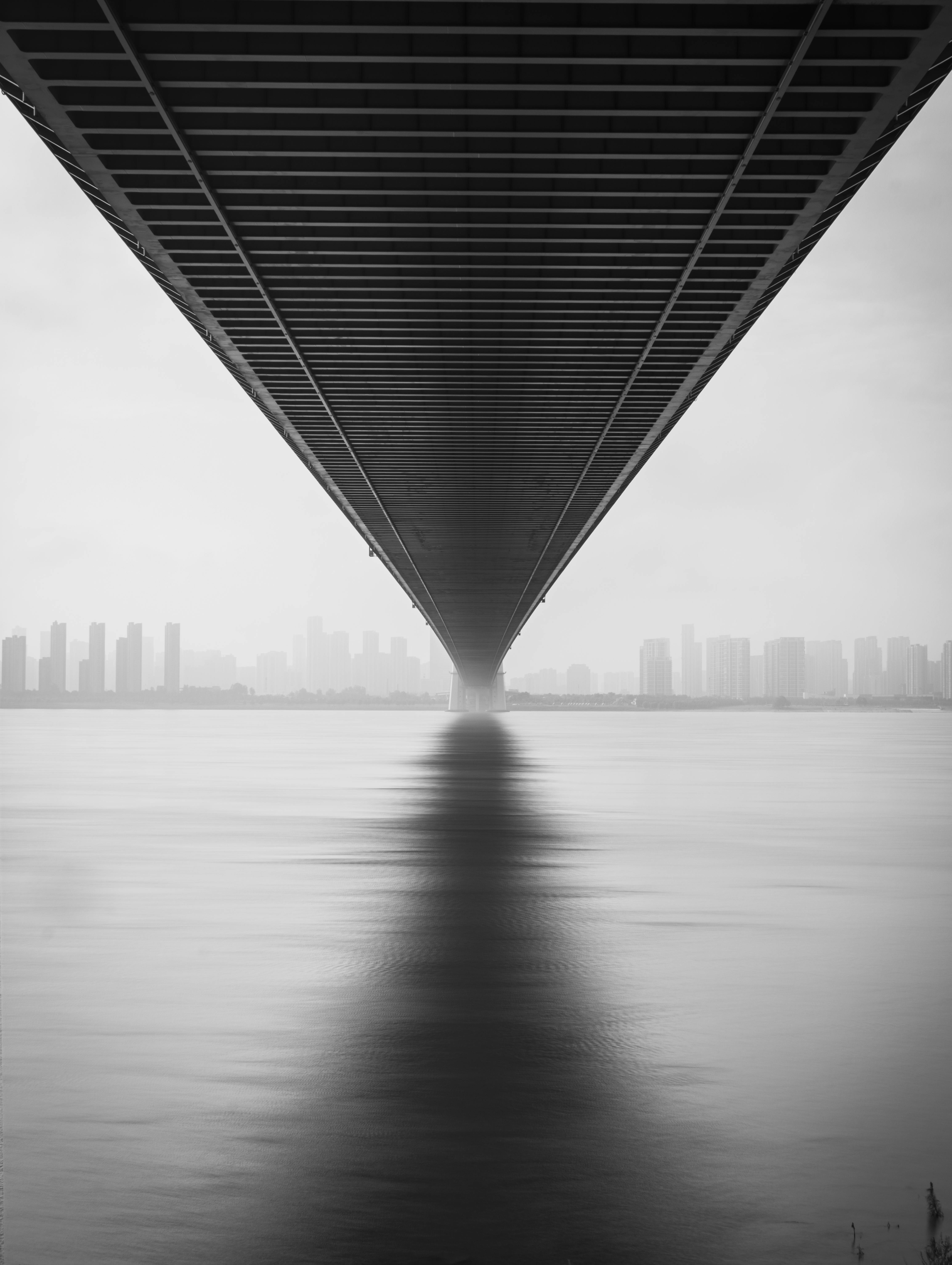 Monochrome image of bridge symmetry and reflection over calm water, showcasing urban architecture.