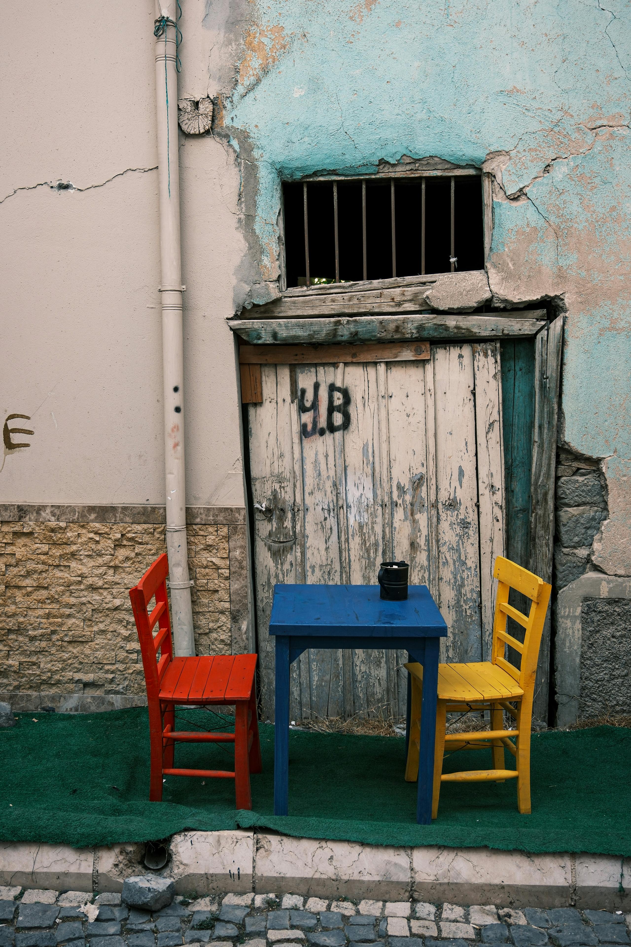 Vibrant red and yellow chairs with a blue table by an old textured wall.