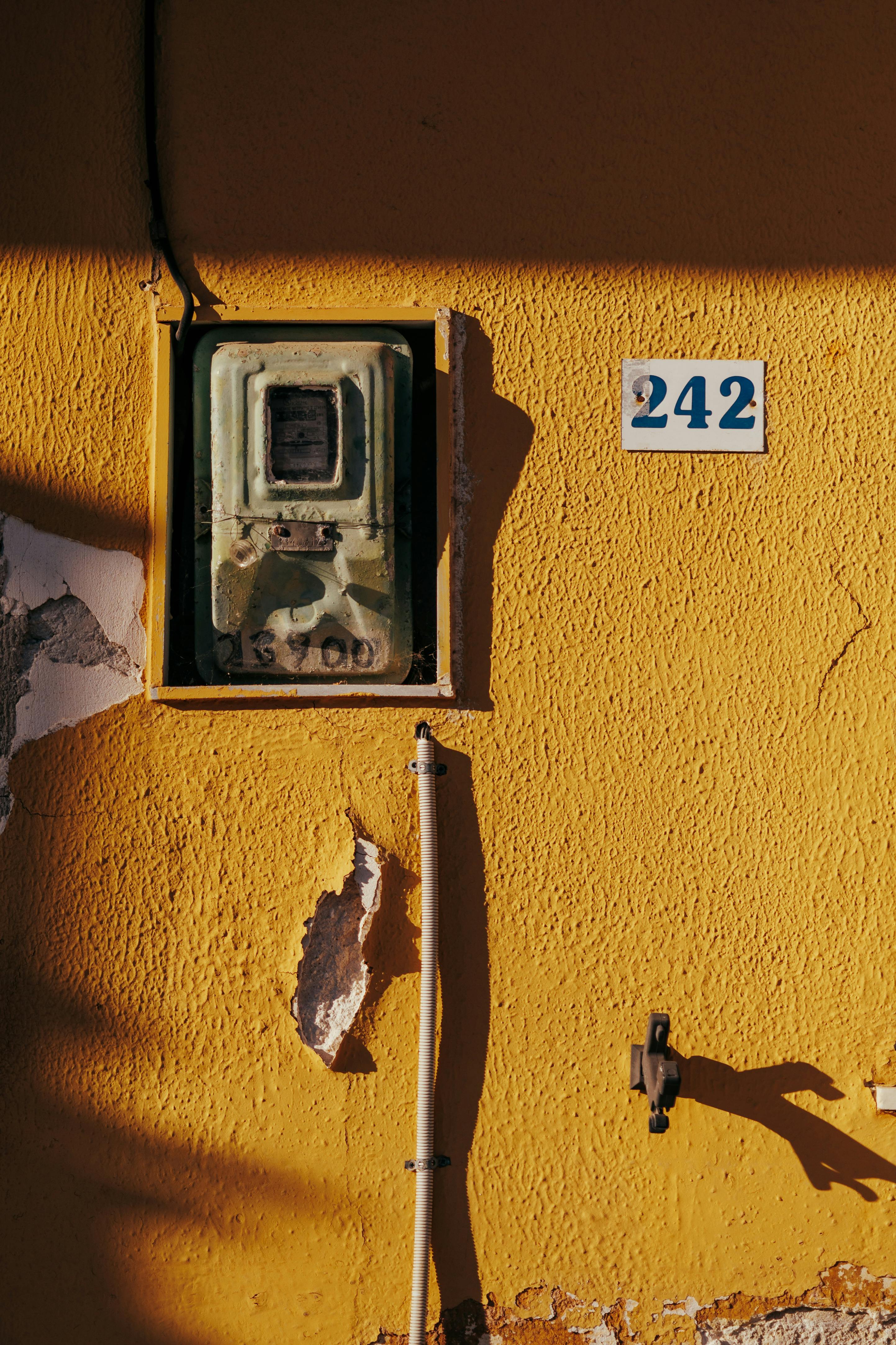 A vintage meter on a textured yellow wall in Keri, Greece with house number 242.