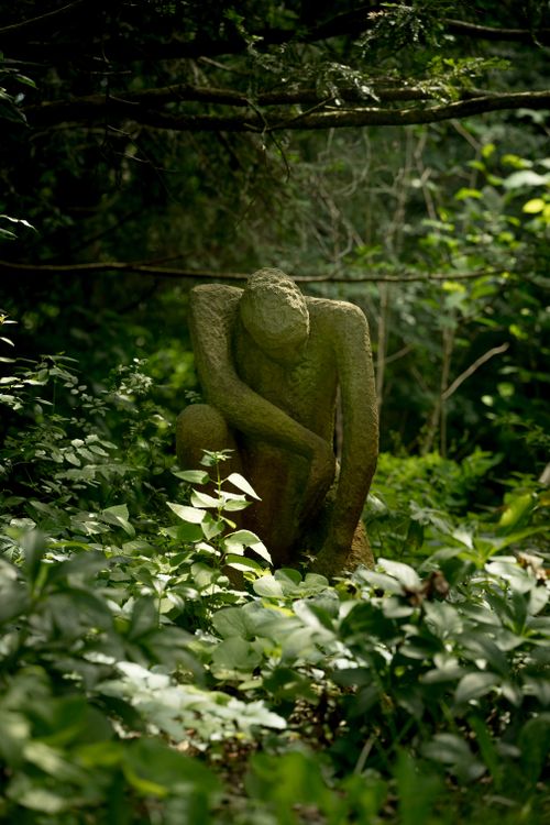 Free A contemplative stone sculpture surrounded by lush green foliage in a peaceful forest setting. Stock Photo