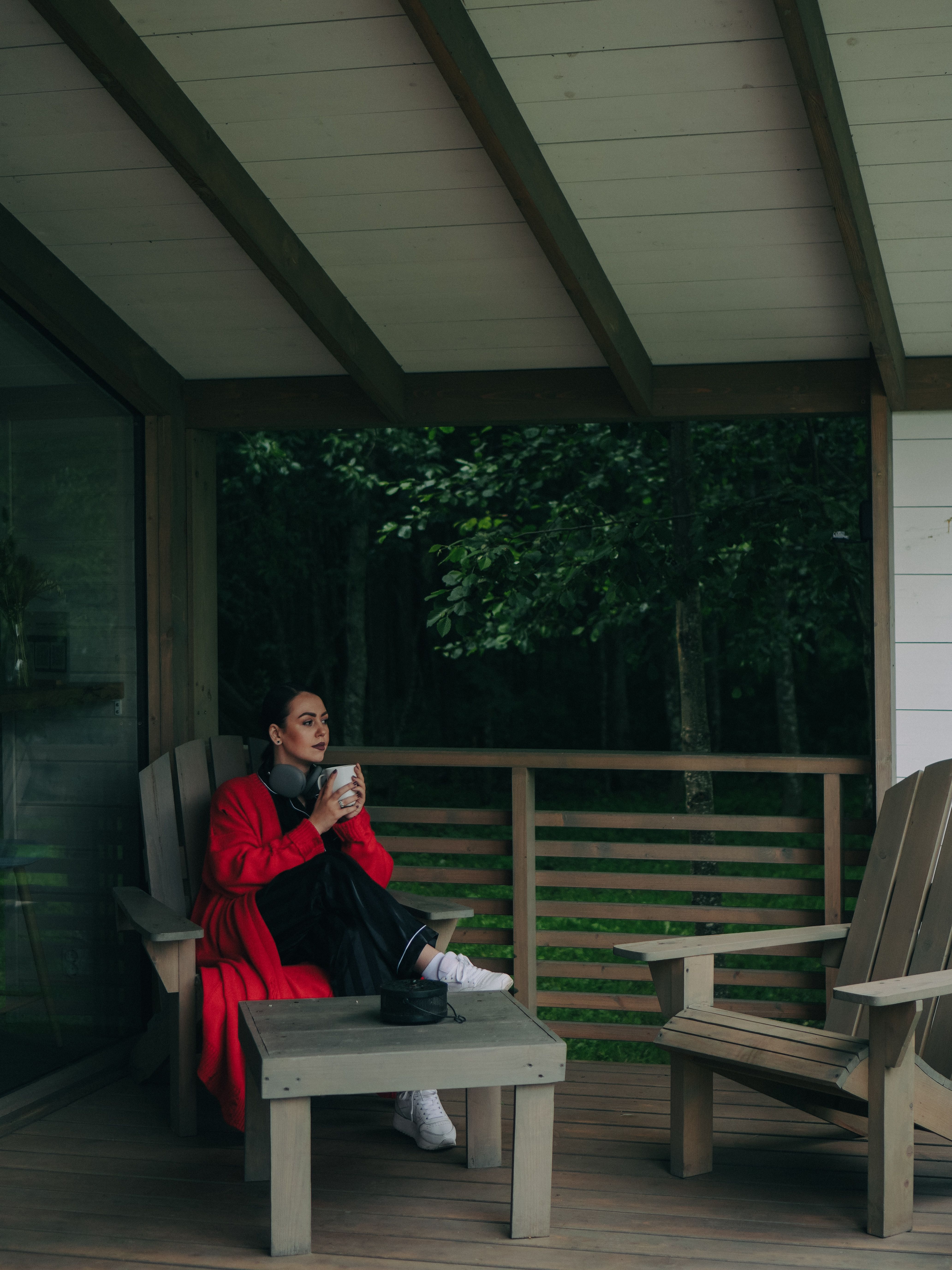 A woman in a red coat sitting on a timber porch with a drink