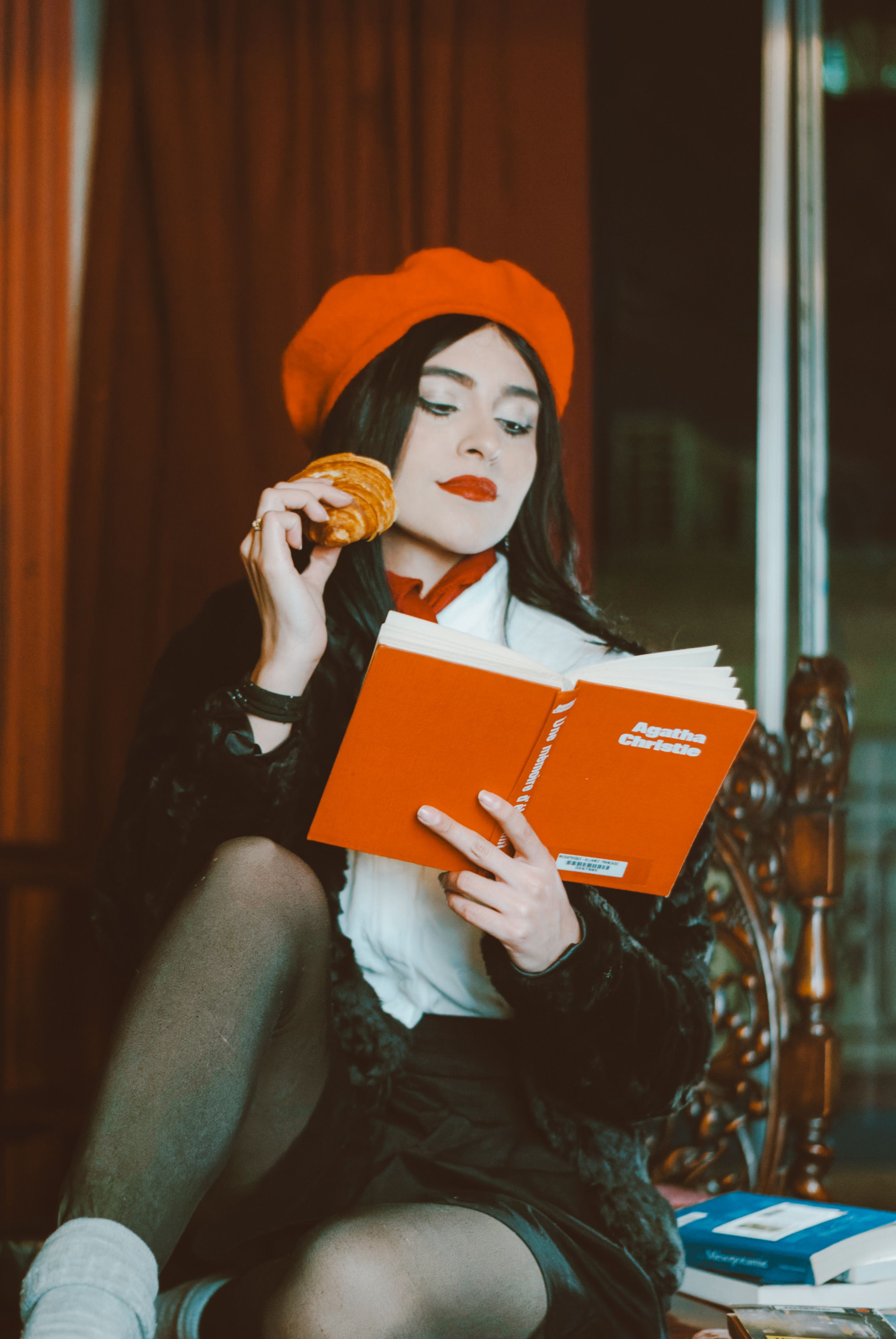 Elegant woman in a beret reading Agatha Christie and enjoying a pastry, indoors.