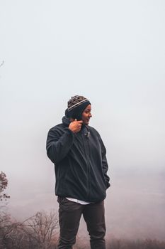 雾气缭绕的户外，一名男子穿着夹克，戴着无檐帽站在那里
