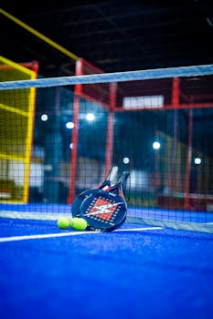 Blue padel court with racket and yellow balls, emphasizing dynamic sports vibe indoors.