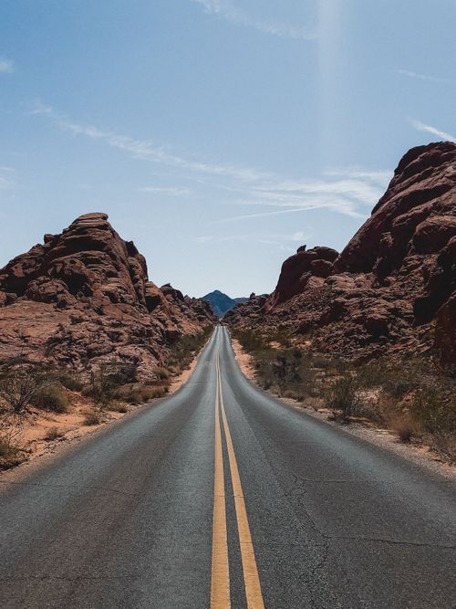 Free Scenic road cutting through dramatic red rock formations under clear blue sky. Stock Photo