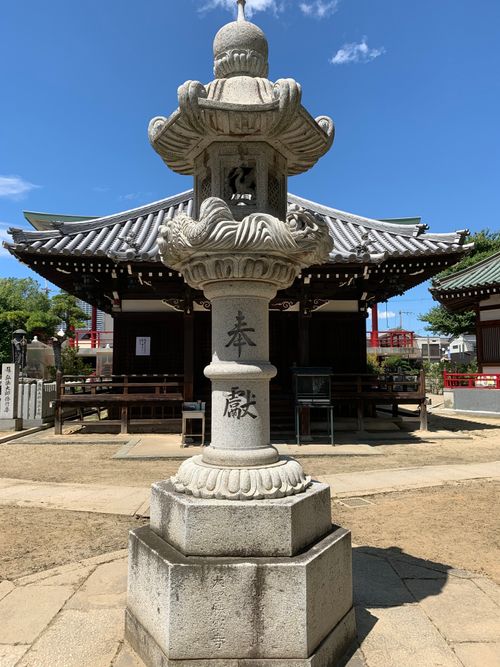 Free A classic Japanese stone lantern stands in a serene temple courtyard under a bright blue sky. Stock Photo