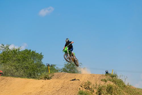 Free Rider performs a high jump on a motocross dirt track under clear blue skies. Stock Photo