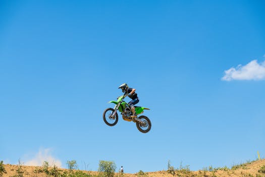 Dynamic image of a motorcyclist in mid-air on a dirt bike, showcasing thrilling motocross action under a clear blue sky.
