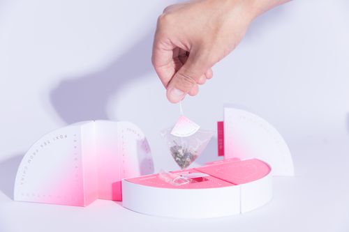 Free A hand holds a designer tea bag above stylish packaging, showcasing modern tea presentation. Stock Photo