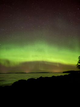 Capture of the vibrant northern lights illuminating the night sky over a serene Finnish lake.