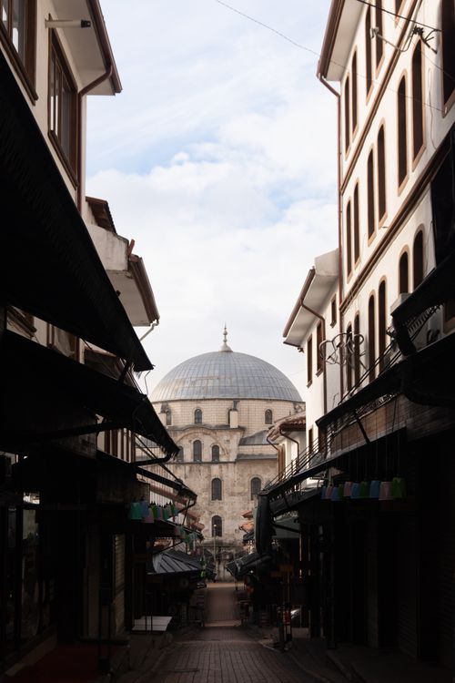 Free Narrow alley leading to a historic mosque dome under a partly cloudy sky. Stock Photo