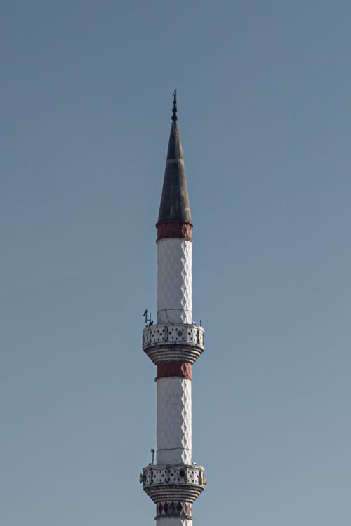 Free A detailed view of a traditional minaret tower set against a clear blue sky, showcasing Islamic architecture. Stock Photo