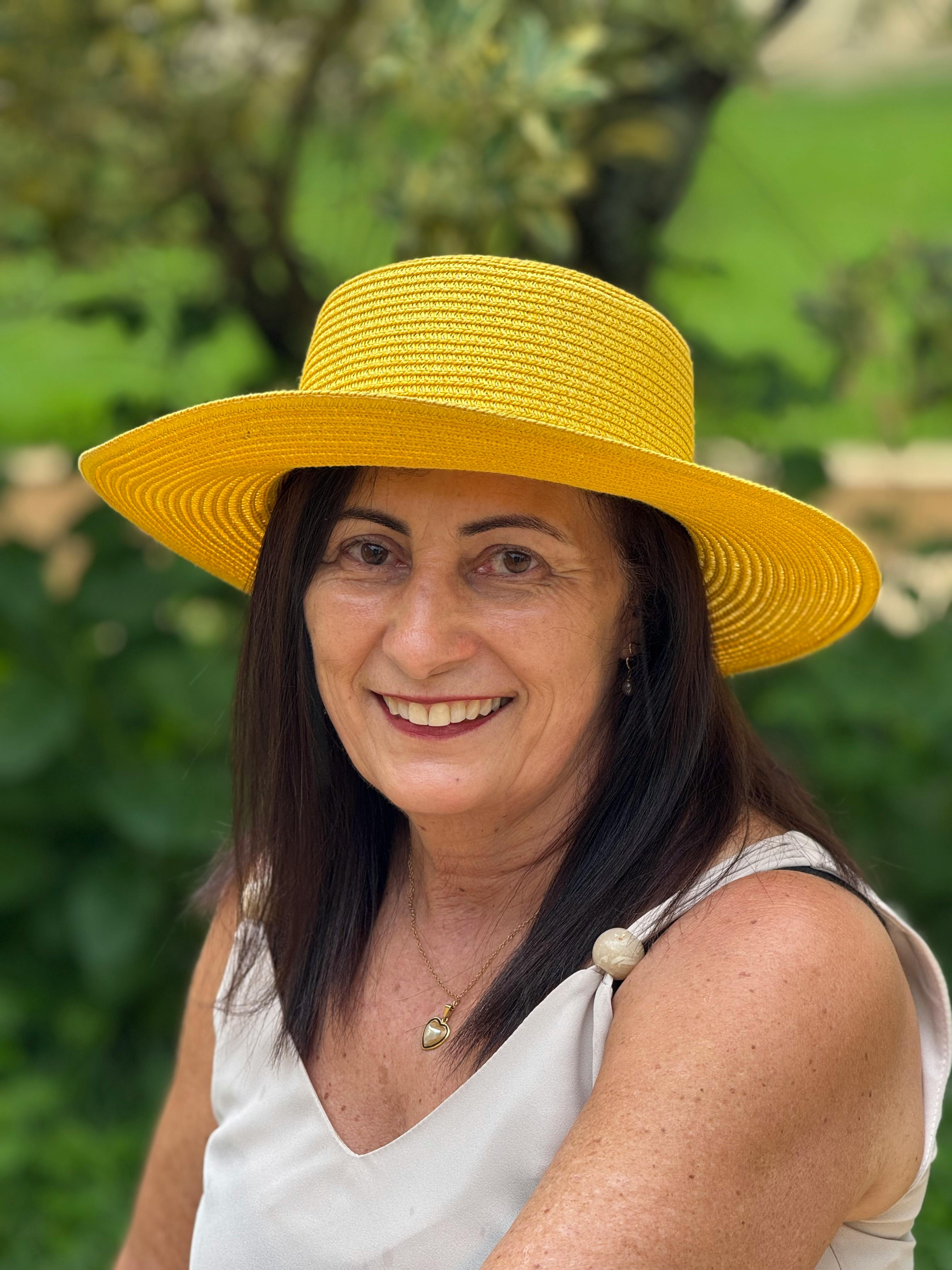 Portrait of a smiling woman in a yellow hat outdoors.