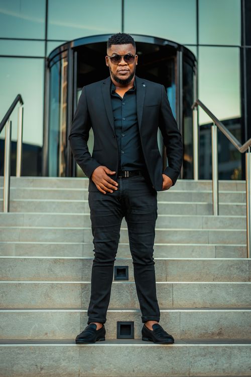 Free Confident businessman in a black suit posing on steps outside a modern building in Pretoria. Stock Photo