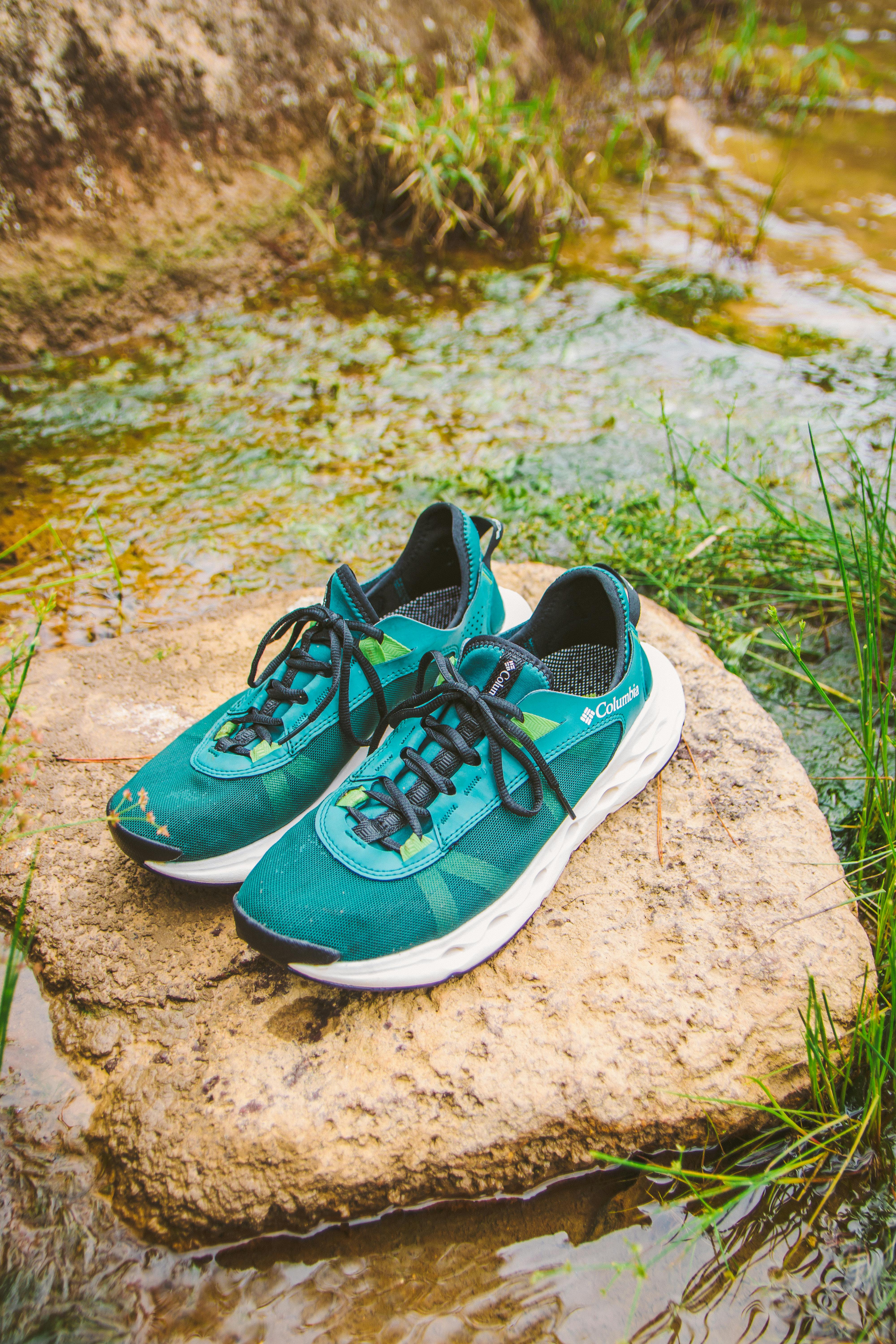 Vibrant green running shoes placed on a rock in a stream, symbolizing adventure.