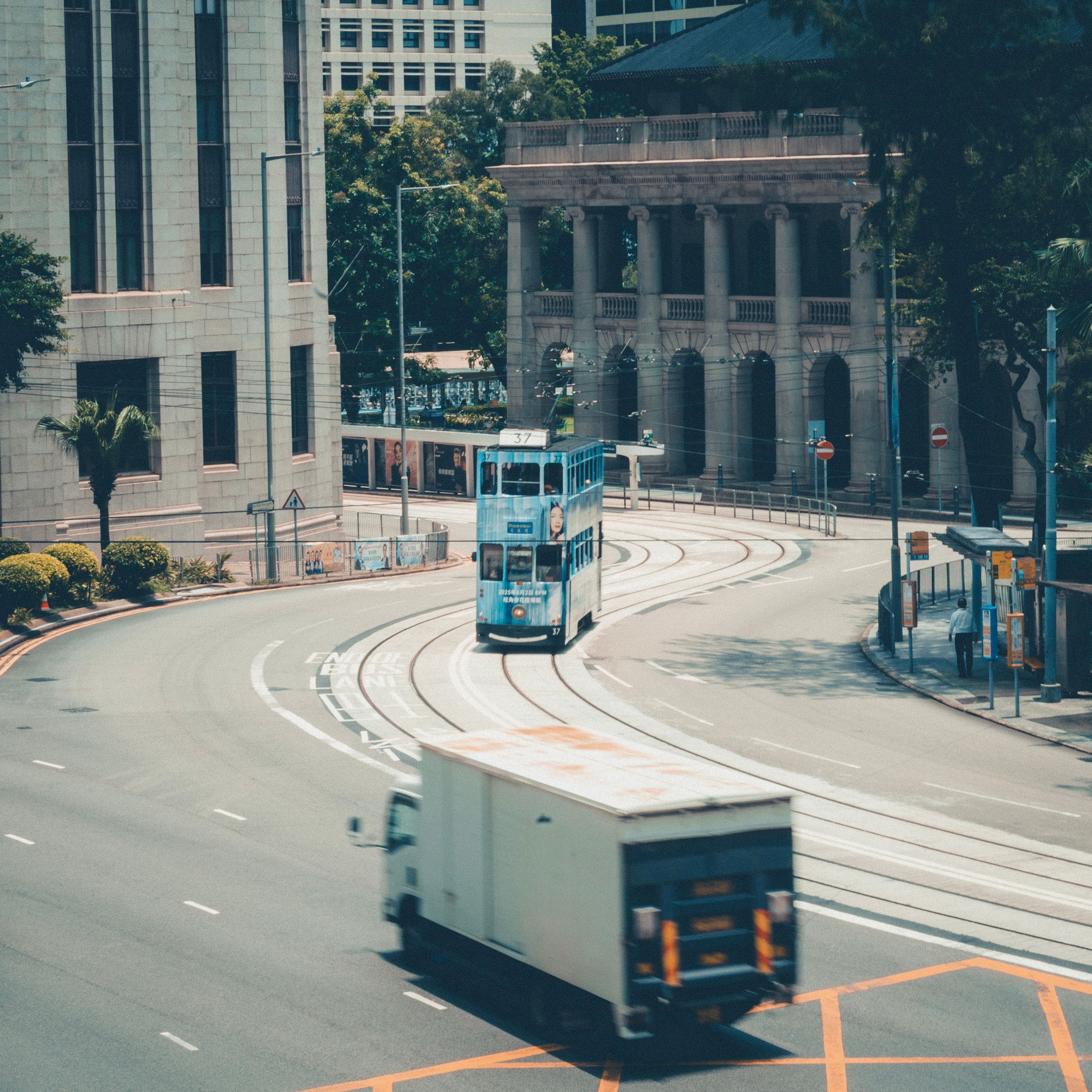 A blue tram travels through an urban cityscape with classic architecture and greenery.