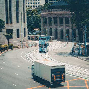 A blue tram travels through an urban cityscape with classic architecture and greenery.
