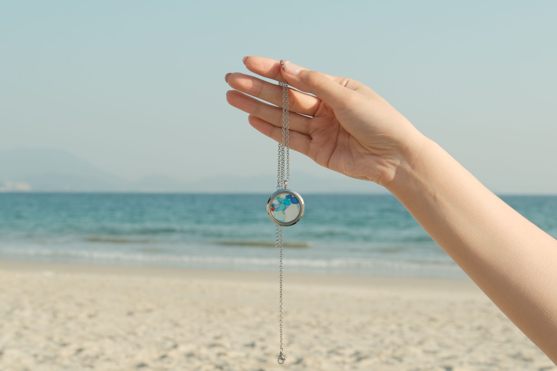 A hand holding a round pendant necklace against a sunny beach background, perfect for lifestyle themes.
