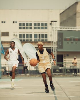 Two young athletes play basketball on an outdoor urban court, showcasing energy and skill.