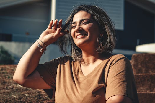 A woman smiling joyfully while sitting outside in natural sunlight.