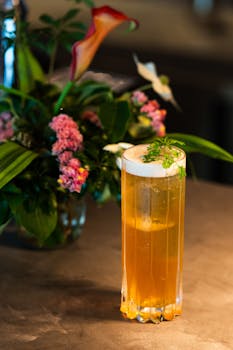 A vibrant yellow cocktail with foam garnish beside a colorful floral arrangement in Tokyo.