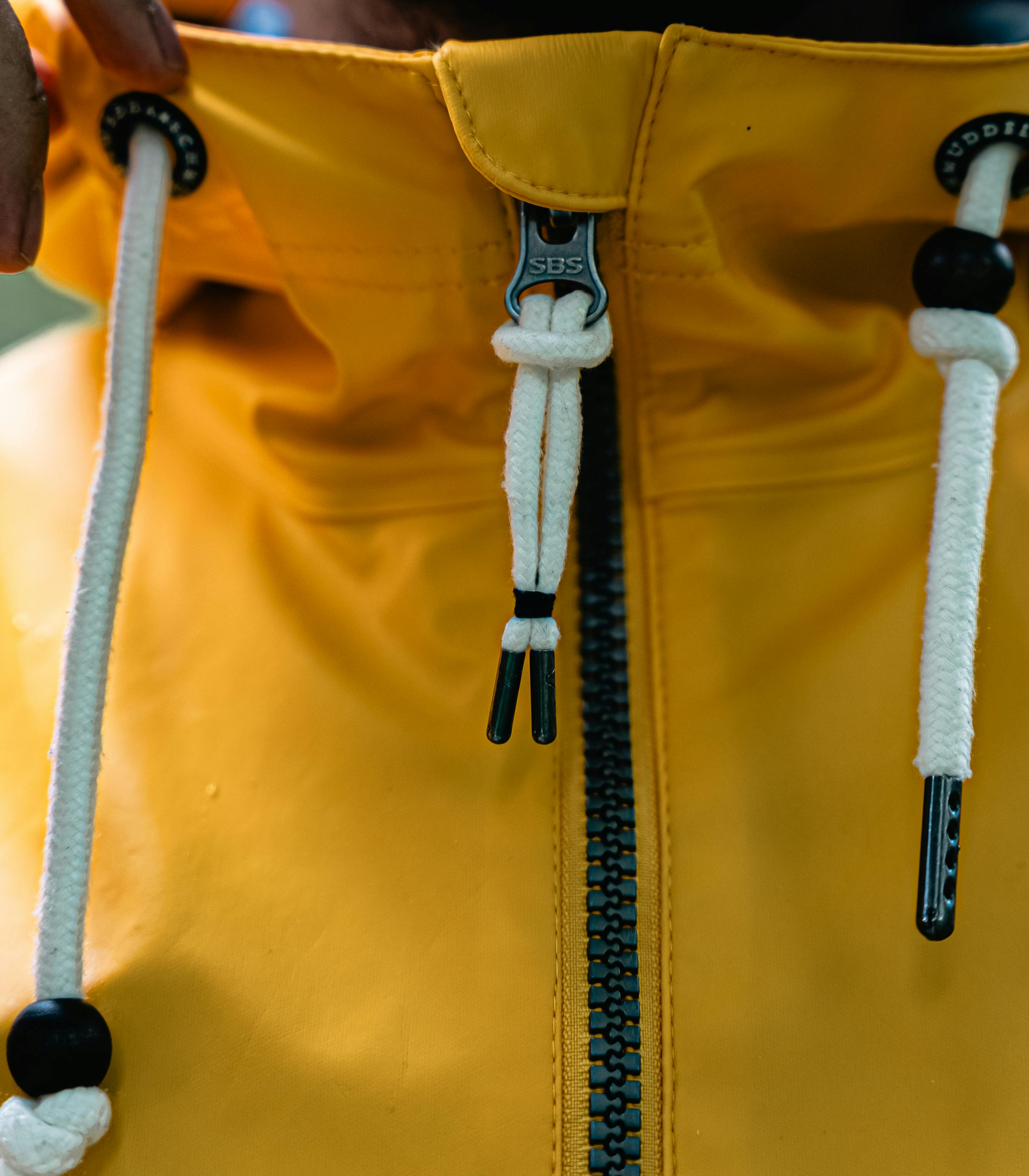 Close-up of a yellow raincoat's zipper and drawstrings, showcasing detail and texture.