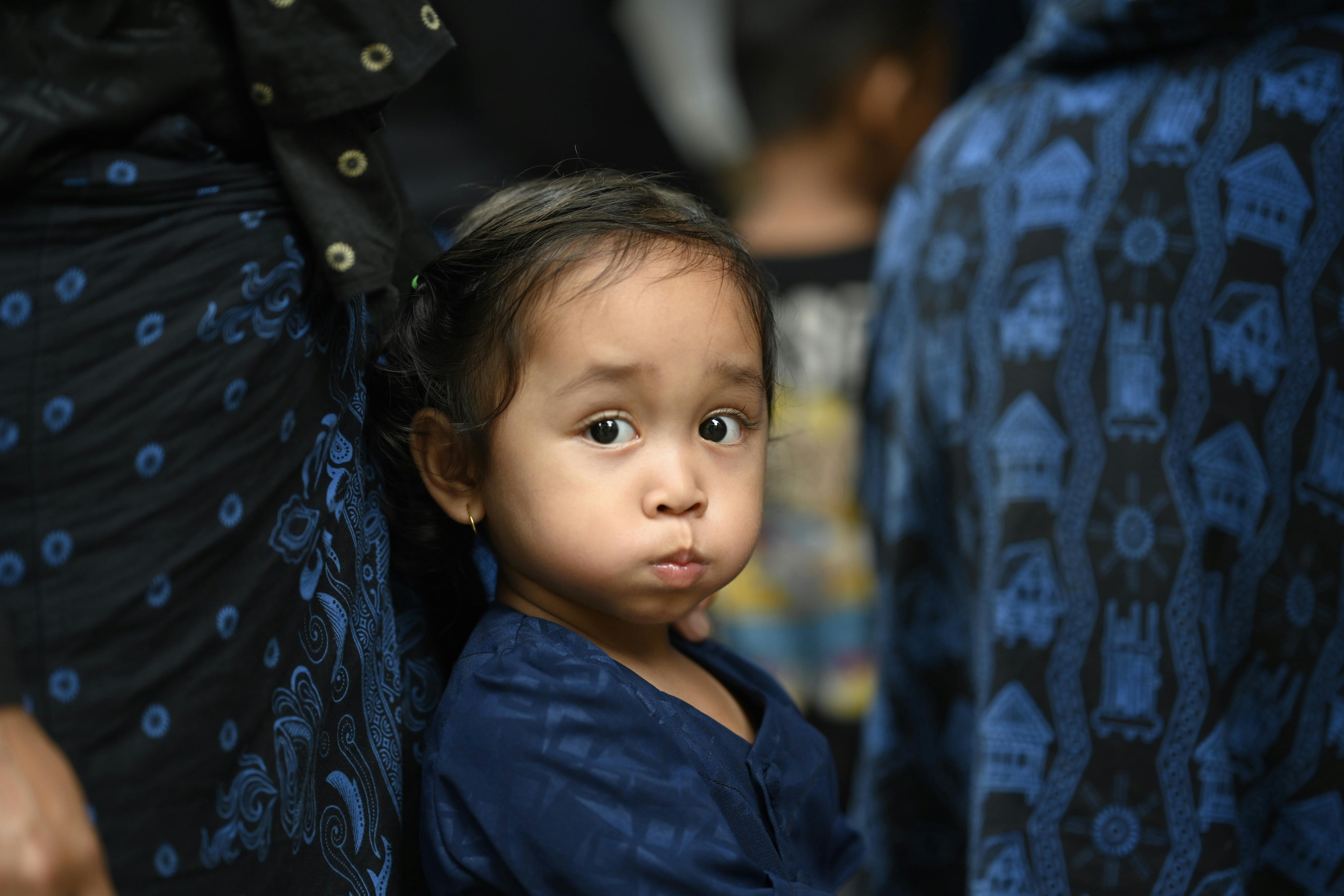 A young child wearing traditional patterned attire looks curiously at the camera, capturing a moment of youthful innocence.