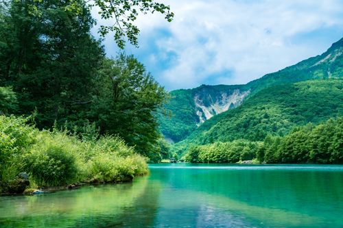 Free Tranquil lake surrounded by lush green mountains under a cloudy sky, offering a peaceful nature scene. Stock Photo