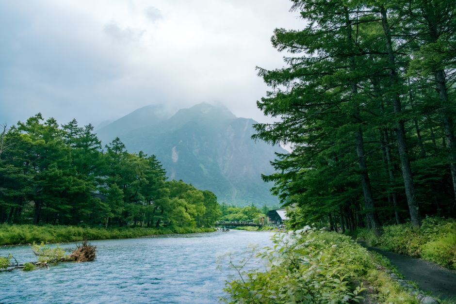 Pristine river flowing through lush forest with majestic mountains in Kamikochi, Japan.