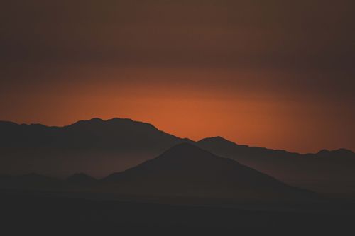 Free Silhouettes of mountains against a vibrant orange sunset sky, creating a dramatic landscape scene. Stock Photo