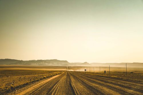 Free A long dirt road stretches through a desolate desert landscape under a clear sky at sunrise. Stock Photo