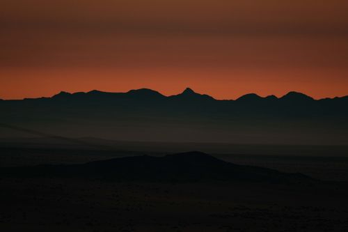 Free Silhouette of mountains with a vibrant orange sky at twilight, creating a dramatic and serene landscape. Stock Photo