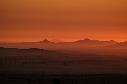 Beautiful desert landscape with mountain silhouettes and orange sunset sky, creating a serene atmosphere.