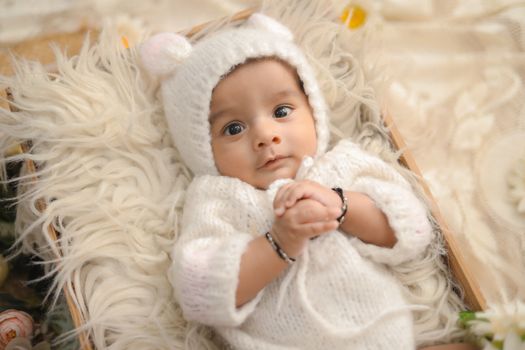 Cute baby wearing a white knitted outfit, lying on soft fur, looking curious and serene.