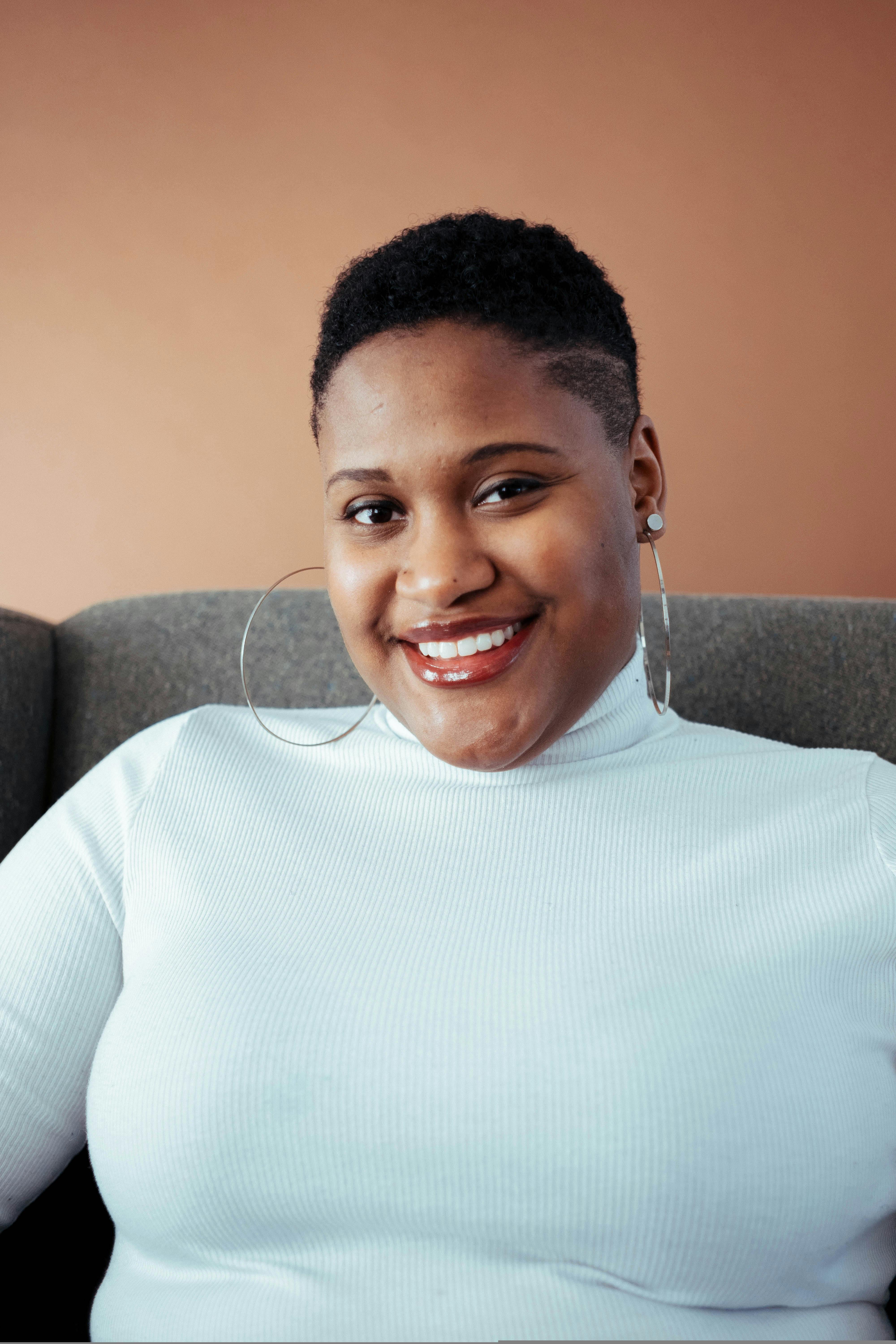 Smiling Woman in White Turtleneck Sweater Sitting on Gray Sofa · Free