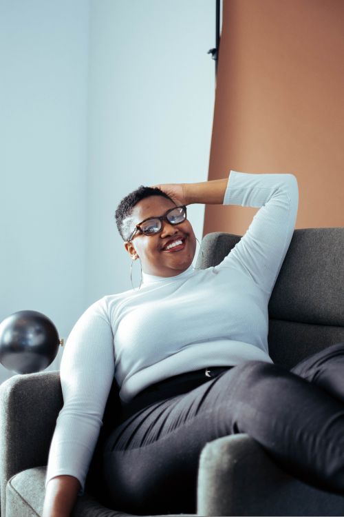 Free Young woman with eyewear relaxing on a chair, showcasing casual fashion in an indoor setting. Stock Photo