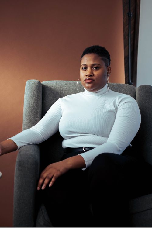 Free Portrait of a confident woman sitting in a modern studio setting, exuding style and poise. Stock Photo