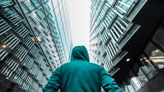 一个穿着连帽衫的人抬头望着城市里光滑反光的摩天大楼