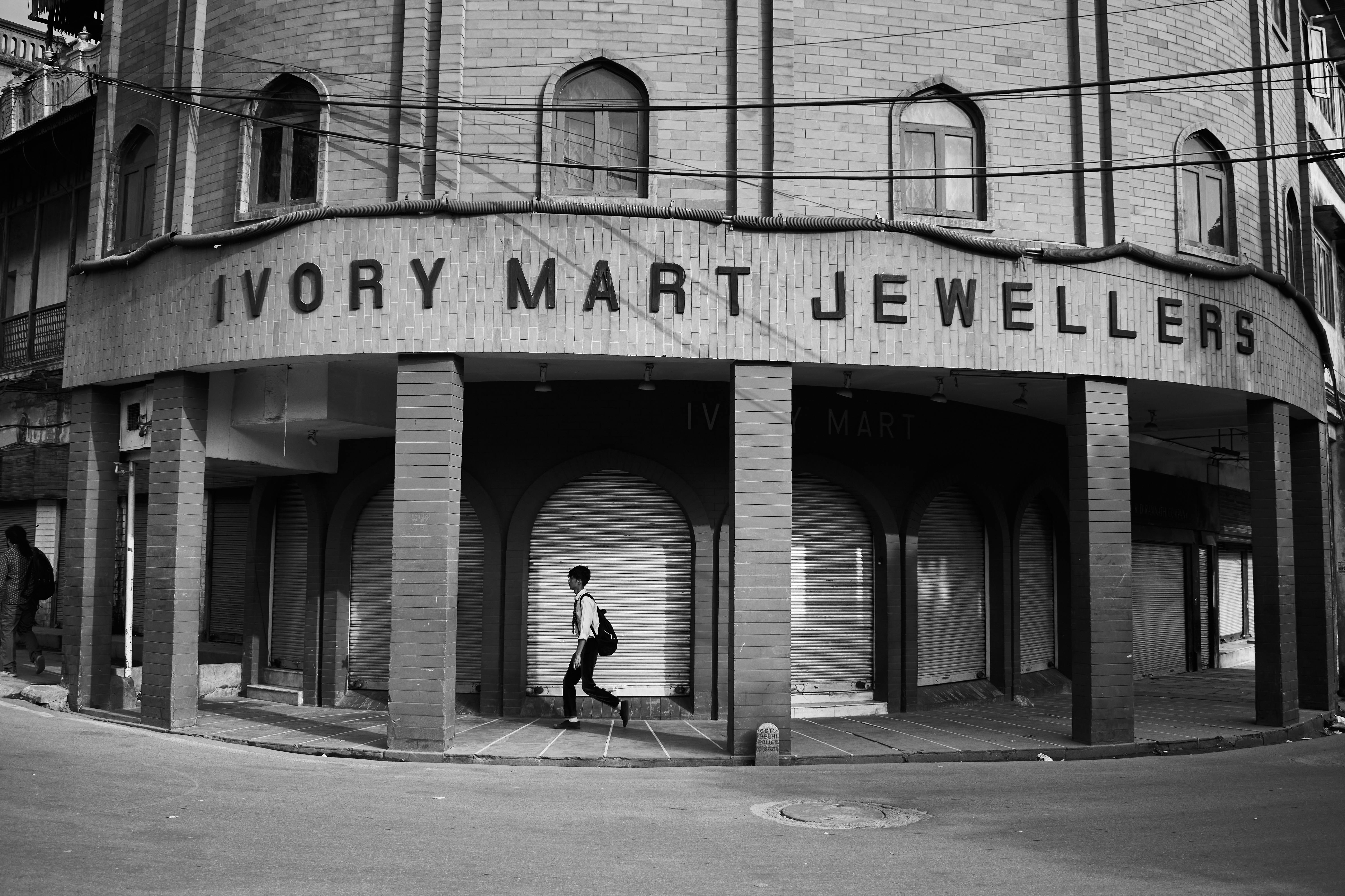 Monochrome photo of a person walking past Ivory Mart Jewellers in Delhi, India.