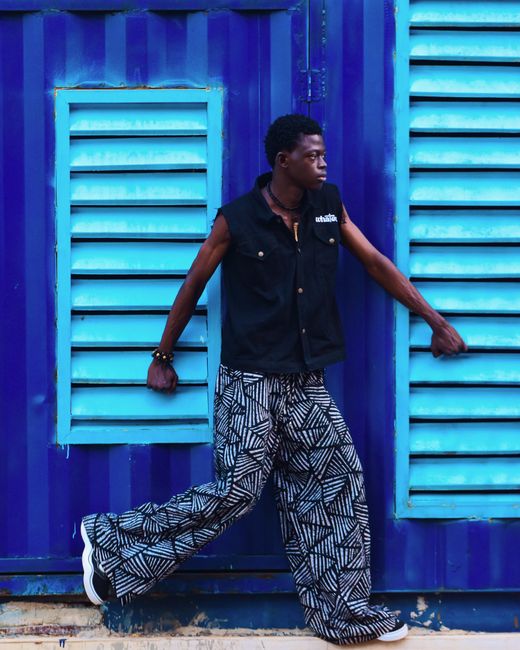 Stylish adult in patterned pants and vest leans against vivid blue shutters.