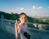 A cheerful young woman posing with a peace sign against a scenic city skyline.